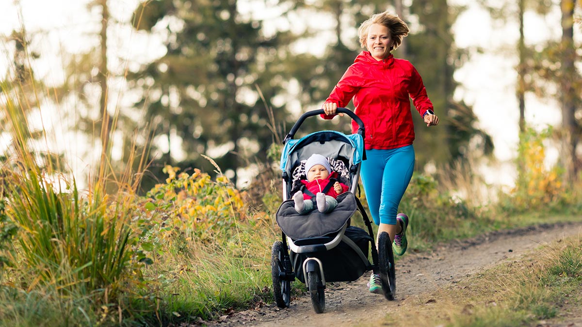 Female Athlete Mother Running On Trail With Her Child In A Running Stroller Smiling