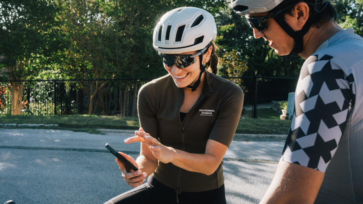 Athlete And Coach Looking At Traininngpeaks Data In Phone On Bikes Together