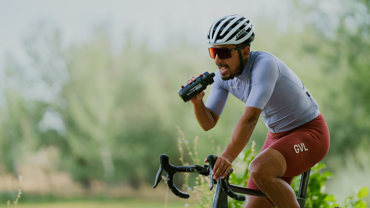 Cycling Athlete Outside On Bike Taking Creatine Supplement From Water Bottle